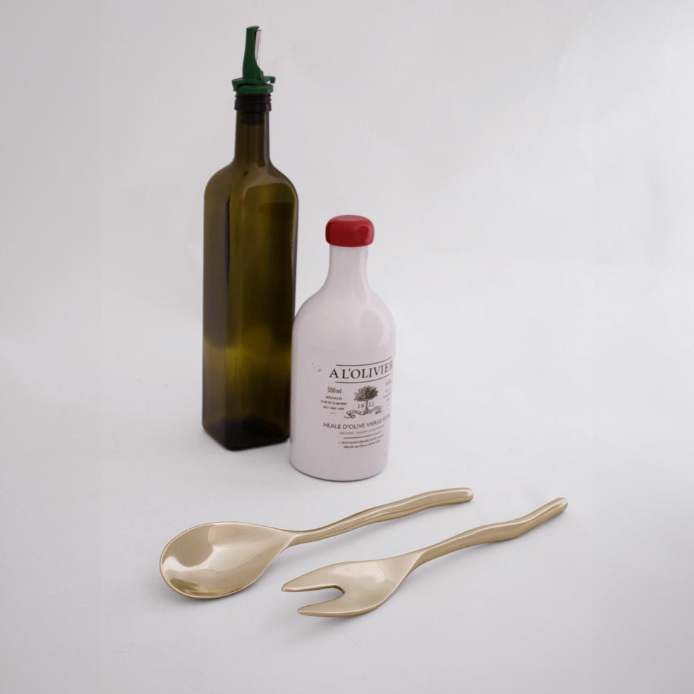 Sierra Modern Maia small salad servers in gold, shown with olive oil bottles on a white background.