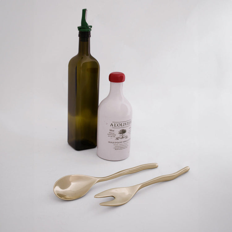 Sierra Modern Maia small salad servers in gold, shown with olive oil bottles on a white background.