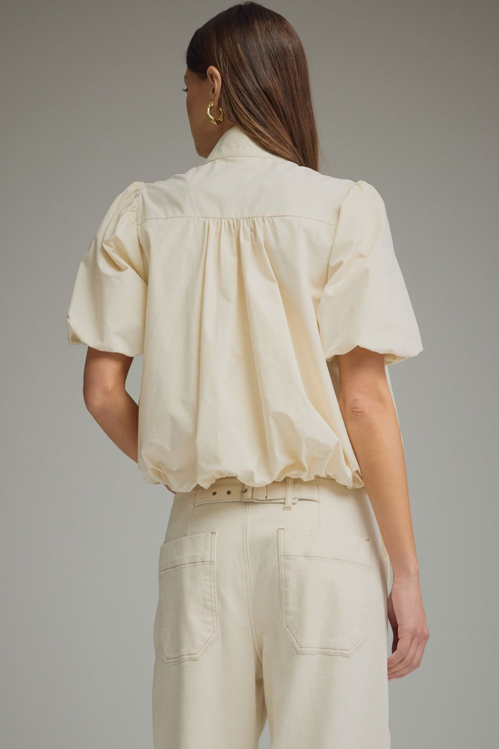 Back view of a woman wearing a cream Jacky short puff sleeve top with a bubble hem and band collar.
