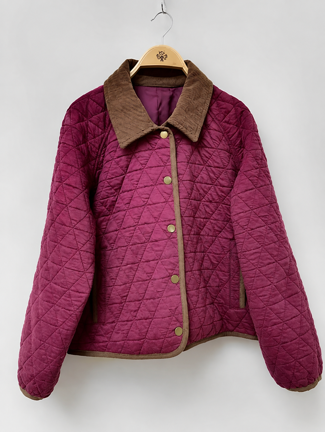 Magenta quilted jacket with a brown corduroy collar and gold snap buttons on a wooden hanger.