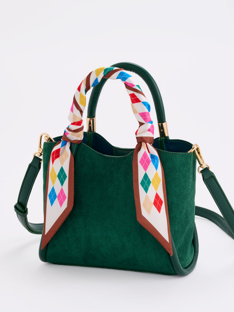 Ivory Argyle Twilly Scarf with colorful diamond pattern wrapped around a green suede handbag handle.