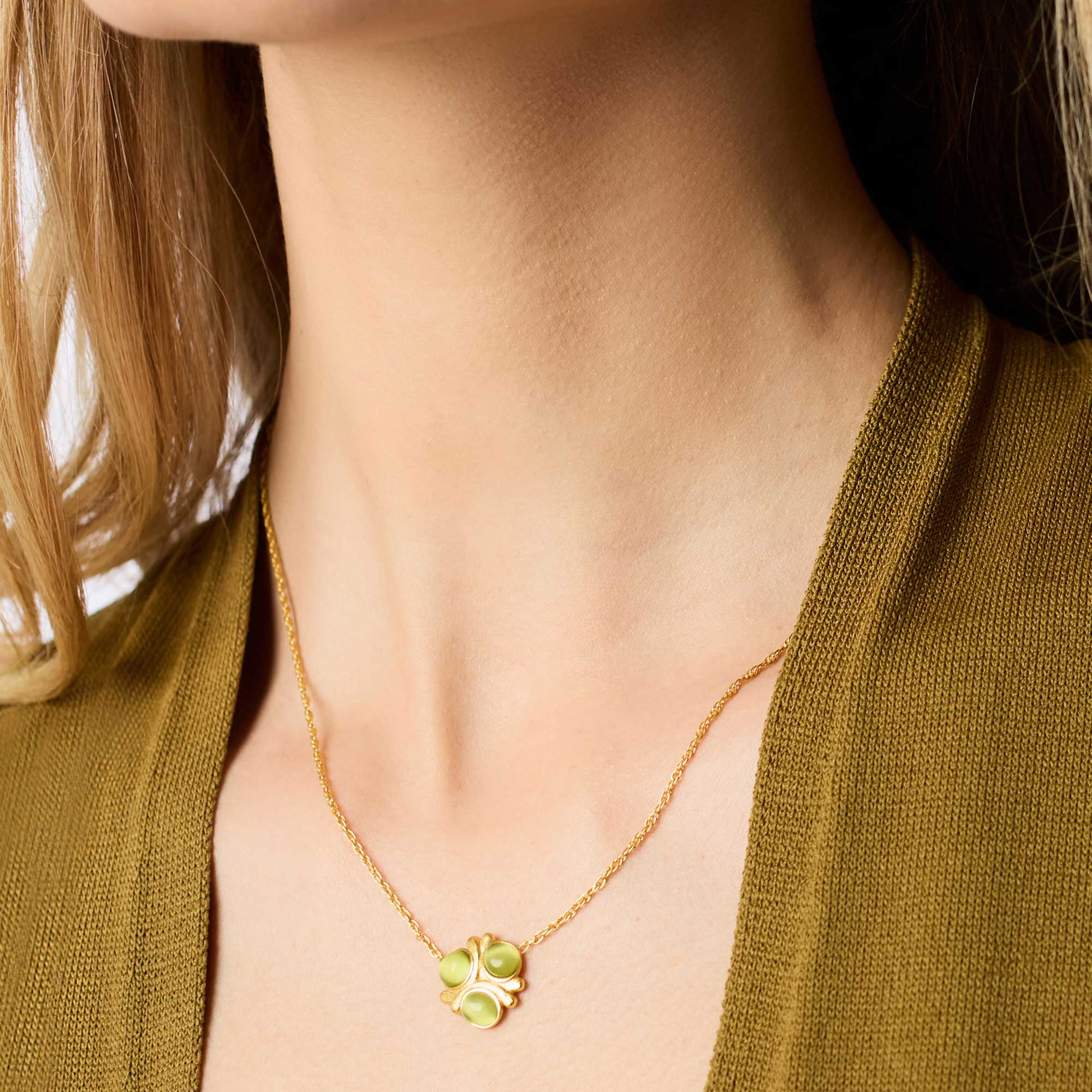 A woman wearing the Cobblestone Delicate Necklace in 24K gold plate with green glass stones.