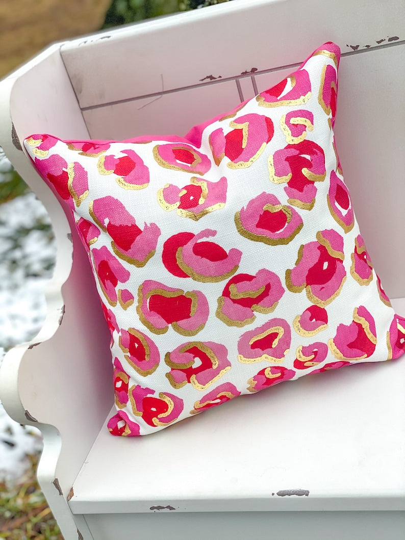 Square decorative pillow with watercolor leopard print in golden pink tones featuring gold foil accents and a velvet backing.
