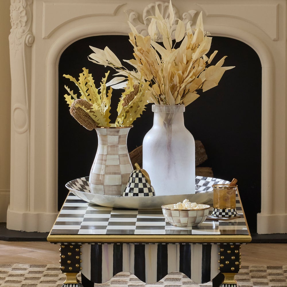 Courtly Check Capiz Decorative Bowl on a checkered table with vases, a pear, and a snack bowl.