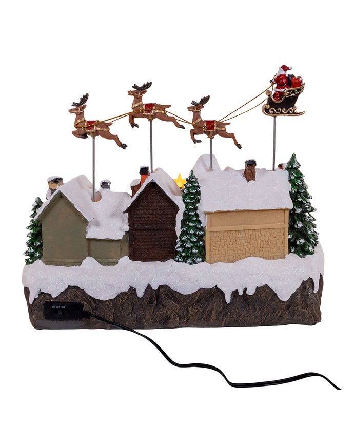 Musical Santa and sleigh table piece with flying reindeer over a snowy village scene.