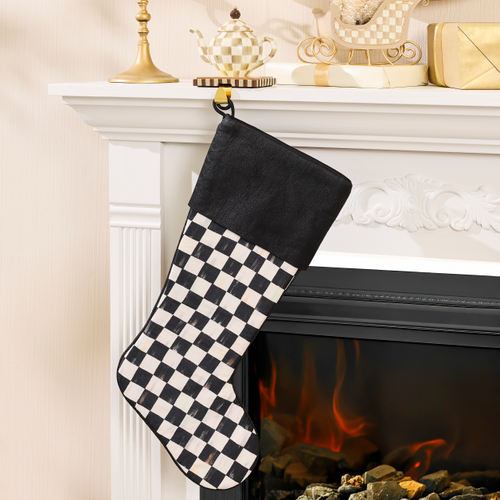Black and white checkered Christmas stocking with a solid black cuff hanging on a white fireplace.