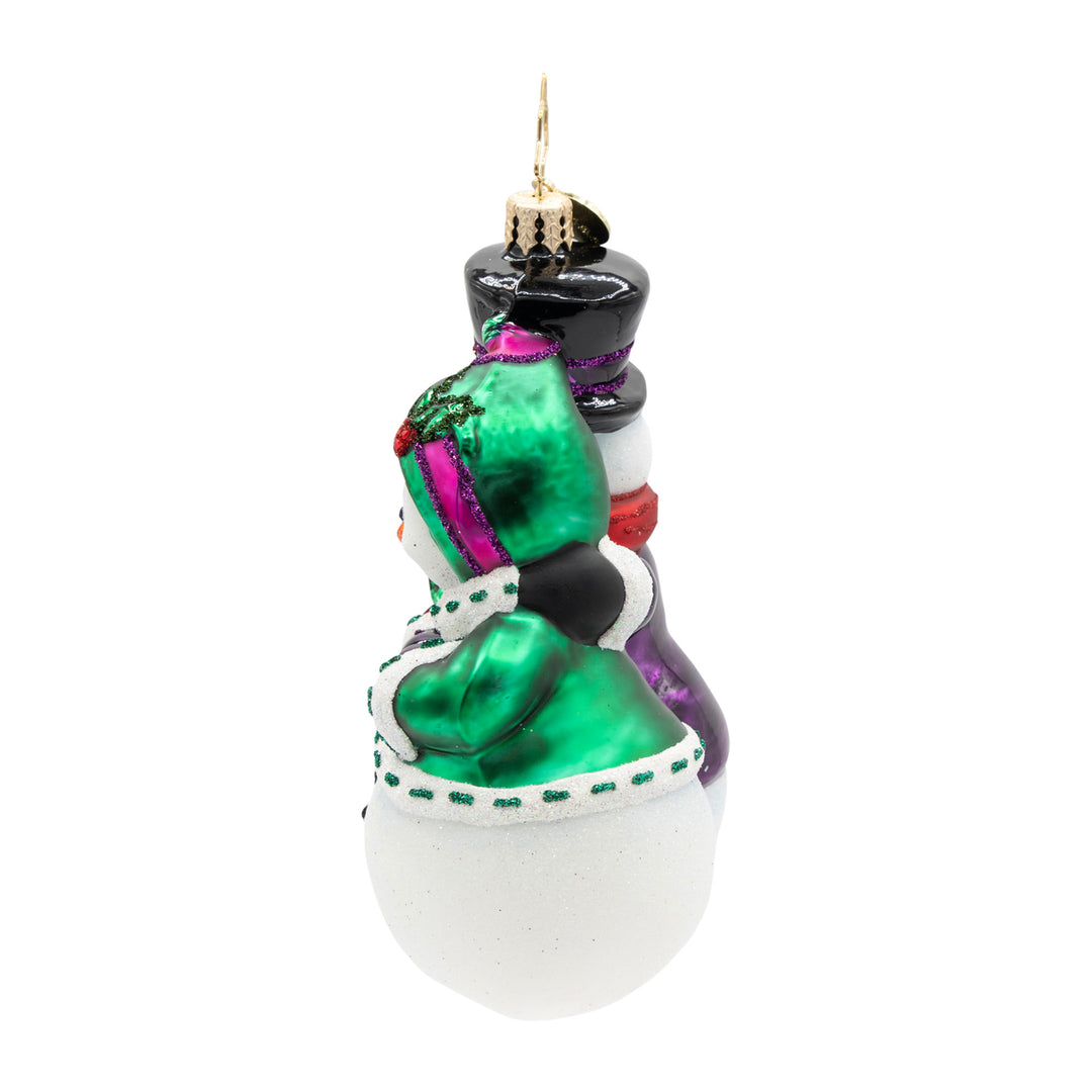 Side view of a glass snow couple ornament featuring a green flocked jacket and black top hat.