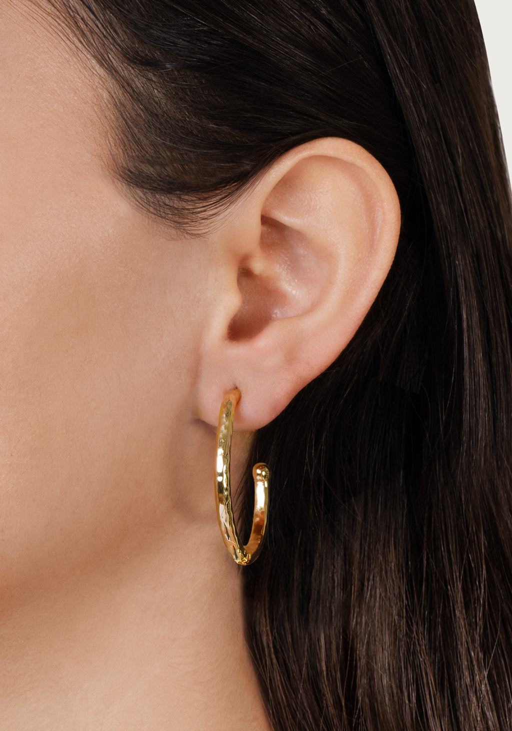 A person wearing a large 18K gold plated brass hoop earring with a hammered, textured finish.