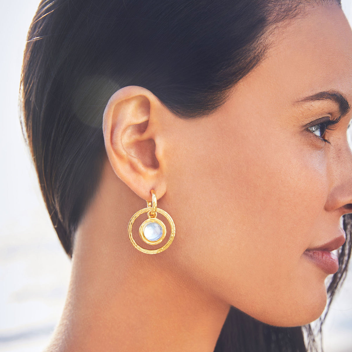 Woman wearing Astor 6-in-1 Charm Earring in 24K gold plate with a blue glass stone.