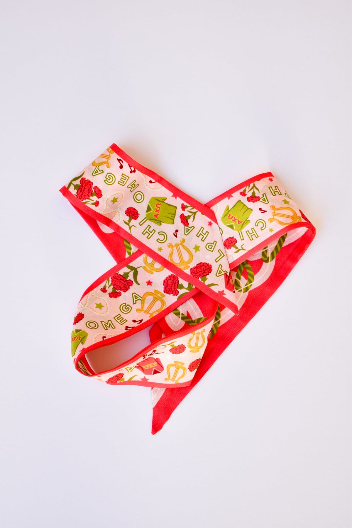 Skinny silk scarf with red borders and a pattern of lyres, flowers, and Alpha Chi Omega text.