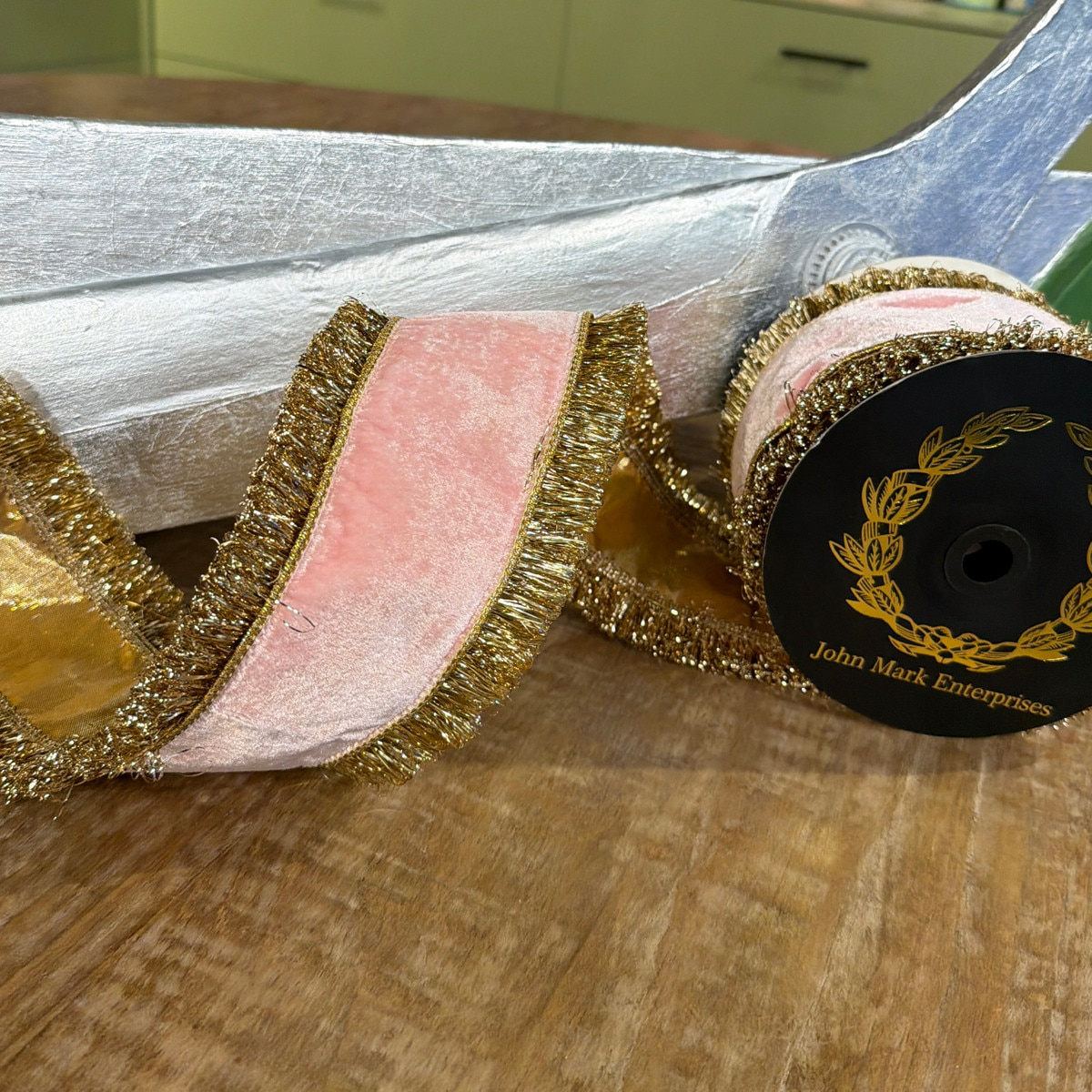 Pink velvet ribbon with gold metallic fringe trim and dupion backing on a black spool.