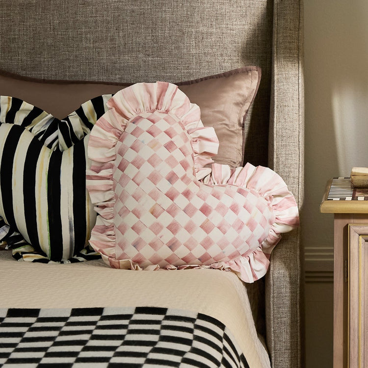 Pink and white checkered heart-shaped throw pillow with a ruffled edge on a bed.