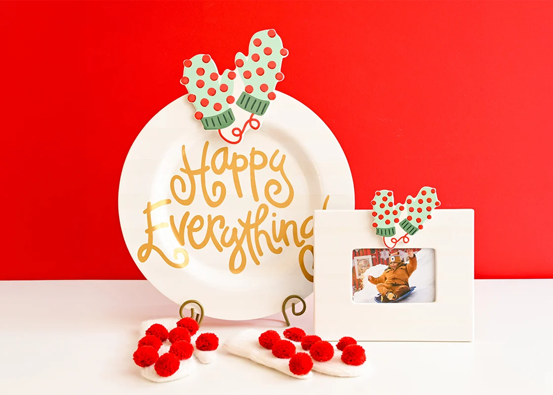 Light green mitten attachment with red polka dots and pom poms on a white plate and frame.