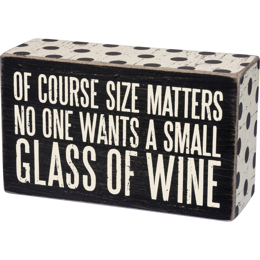Black wooden box sign with white polka dots and text: "OF COURSE SIZE MATTERS NO ONE WANTS A SMALL GLASS OF WINE."