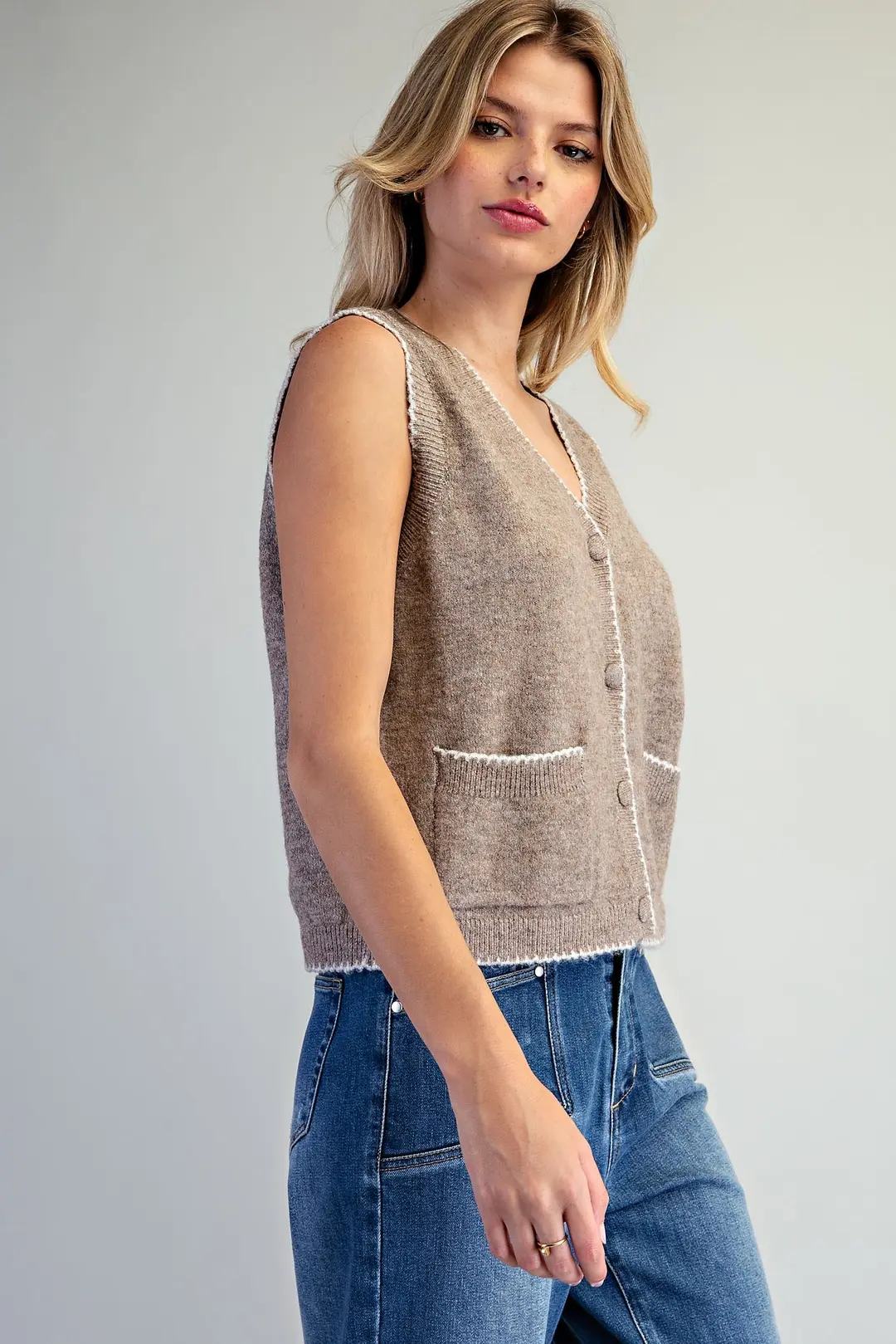 Celeste sleeveless knit vest in taupe with white whipstitch trim, button front, and patch pockets.