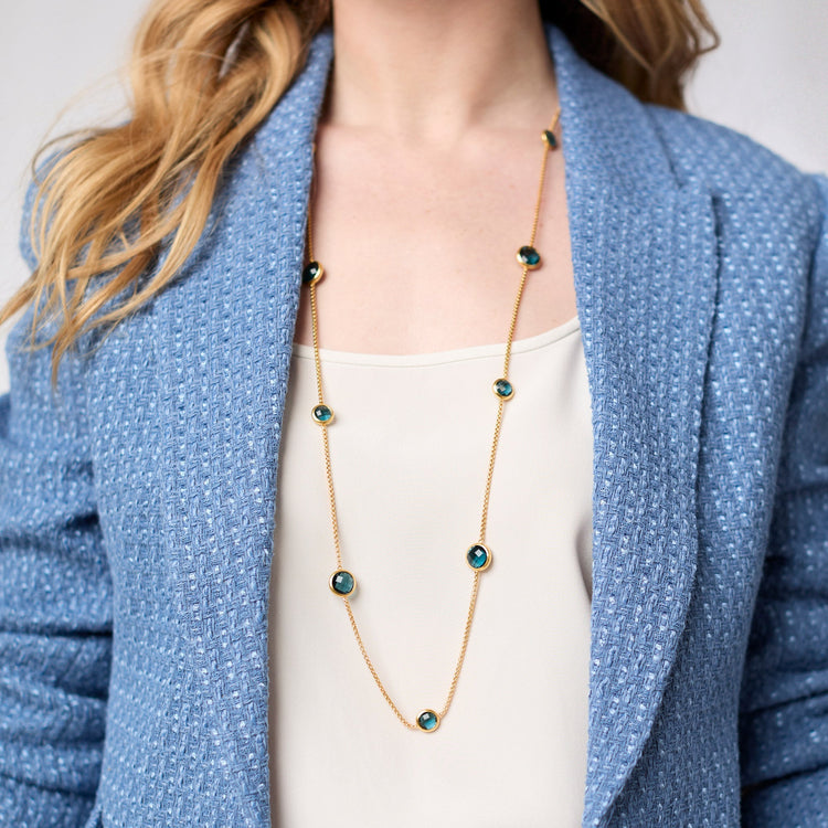 A long 24K gold plated station necklace with teal glass stones worn over a blue tweed blazer.