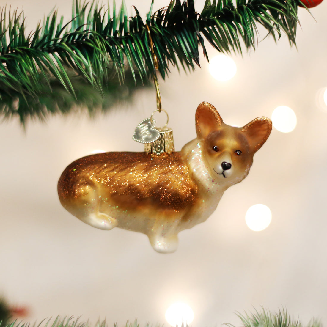 Glittery glass Pembroke Welsh Corgi Christmas ornament hanging from a green pine tree branch.