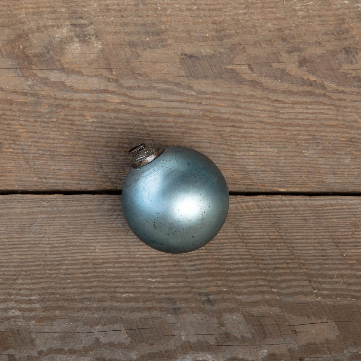 Antique matte blue kyanite glass ball ornament on a rustic wood surface.