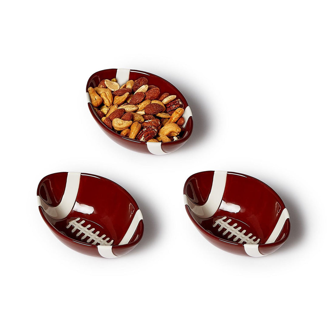 Three football-shaped ceramic tidbit bowls in maroon and white, one filled with mixed nuts.