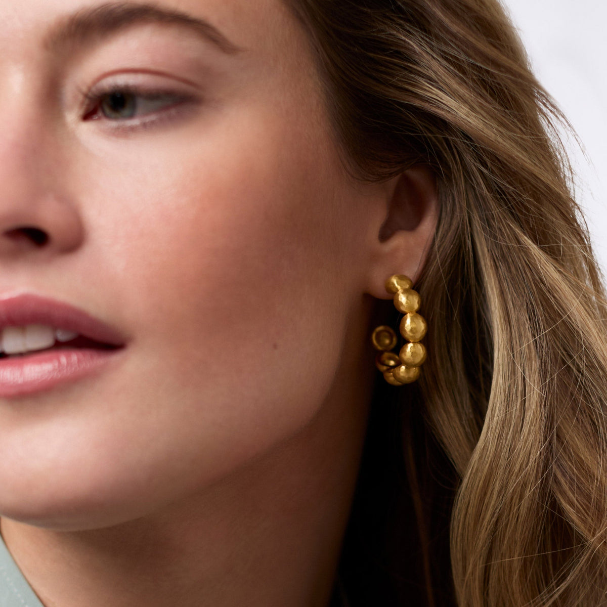 Close-up of a woman wearing a Solara Nova Hoop Gold earring with a textured, beaded design.