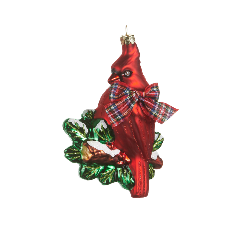 Red glass cardinal ornament perched on holly leaves with a plaid bow and glittery snow accents.