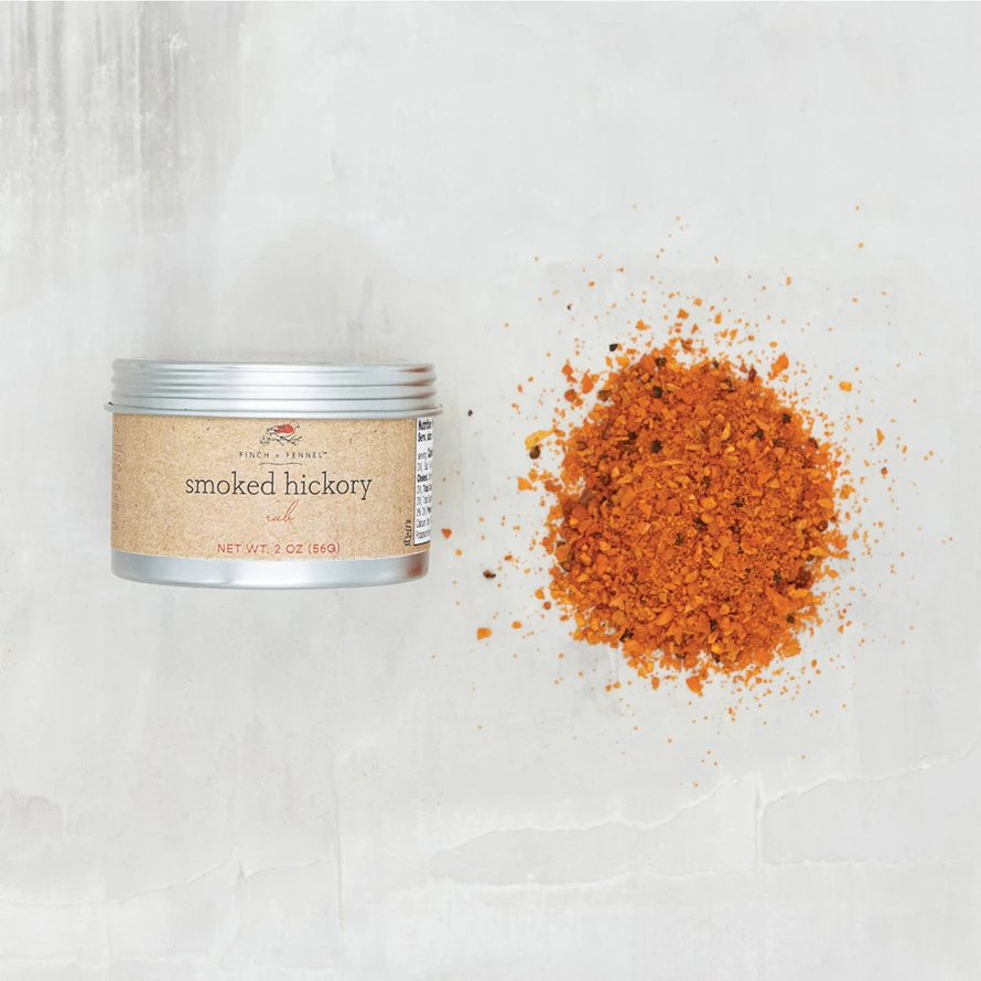 Smoked Hickory Rub in a 2 oz metal tin next to a pile of the orange-brown spice blend.