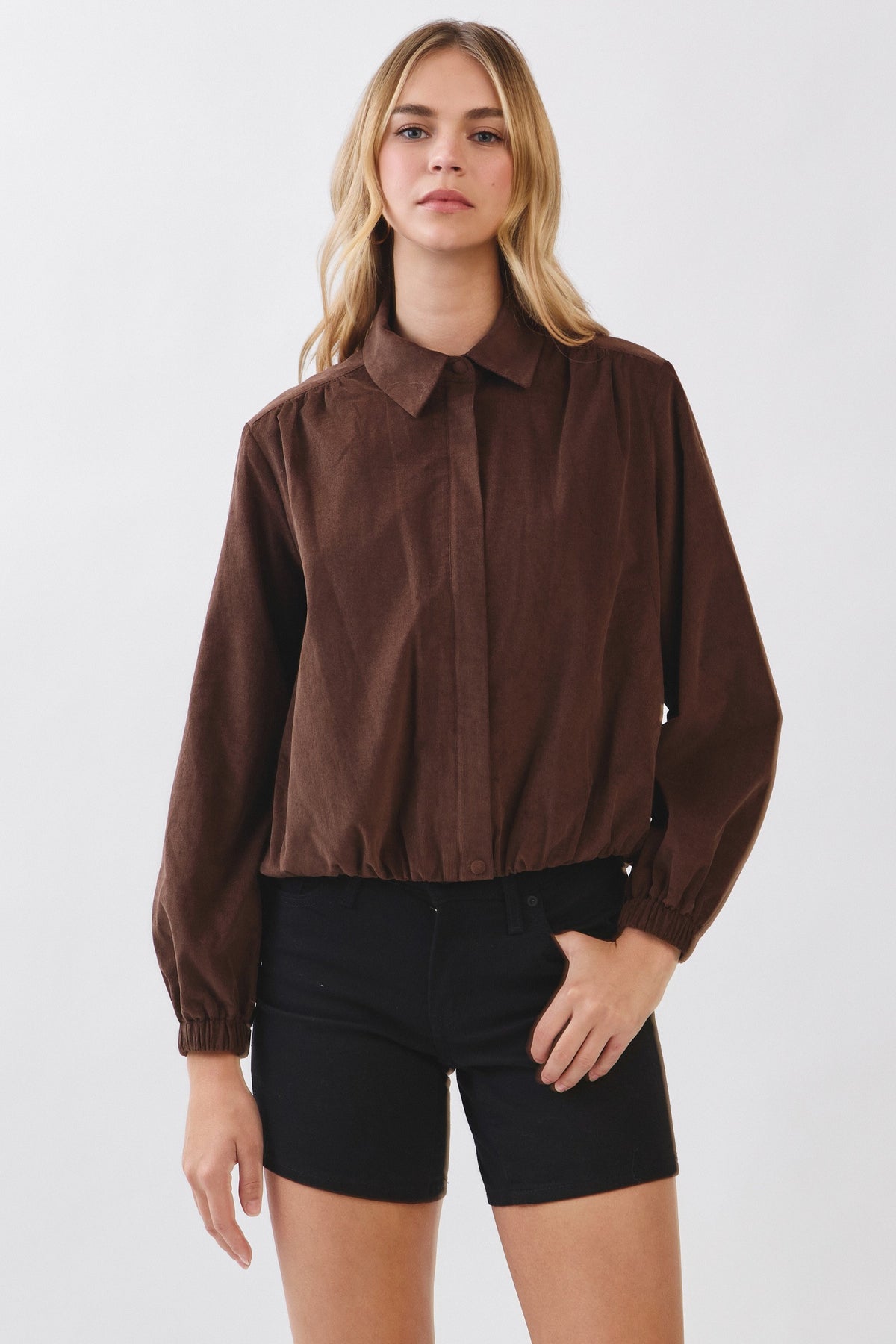 Woman wearing a brown corduroy zip-up collar jacket with elasticated hem and cuffs.