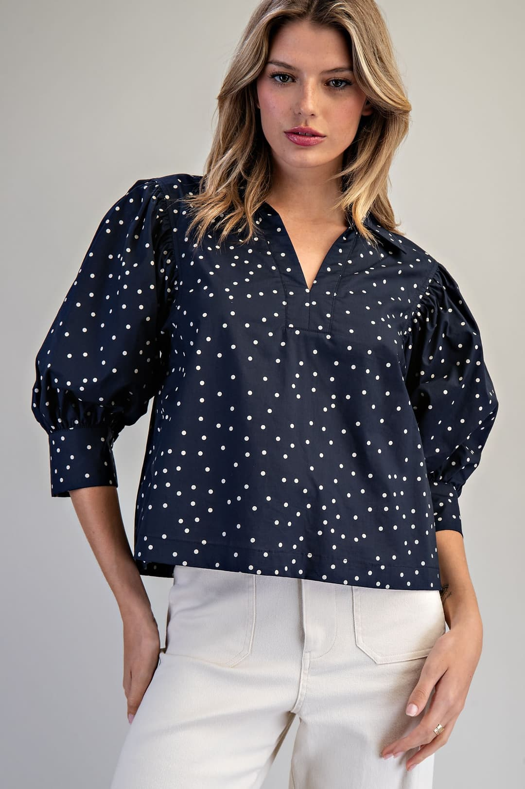 Woman wearing a navy blue Molly Polka Dot Puff Sleeve Blouse with white pants.