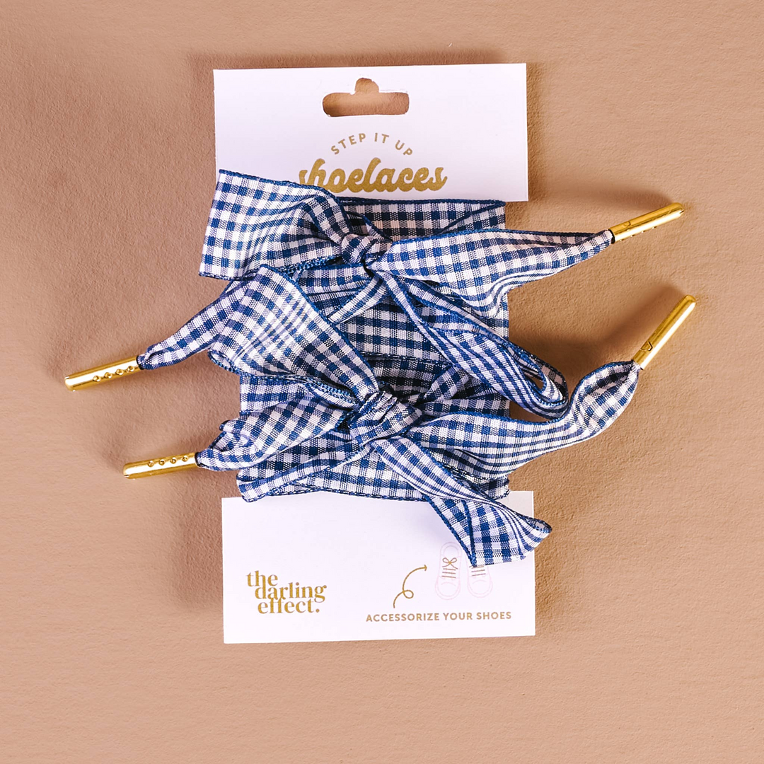 Blue and white gingham shoelaces with gold metal aglets on a white display card.