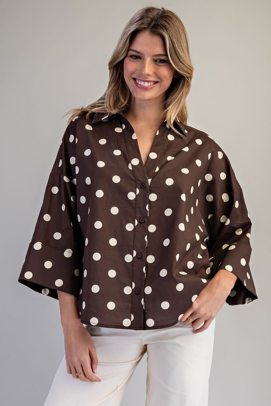 Woman wearing a brown oversized button-down blouse with white polka dots and wide dolman sleeves.