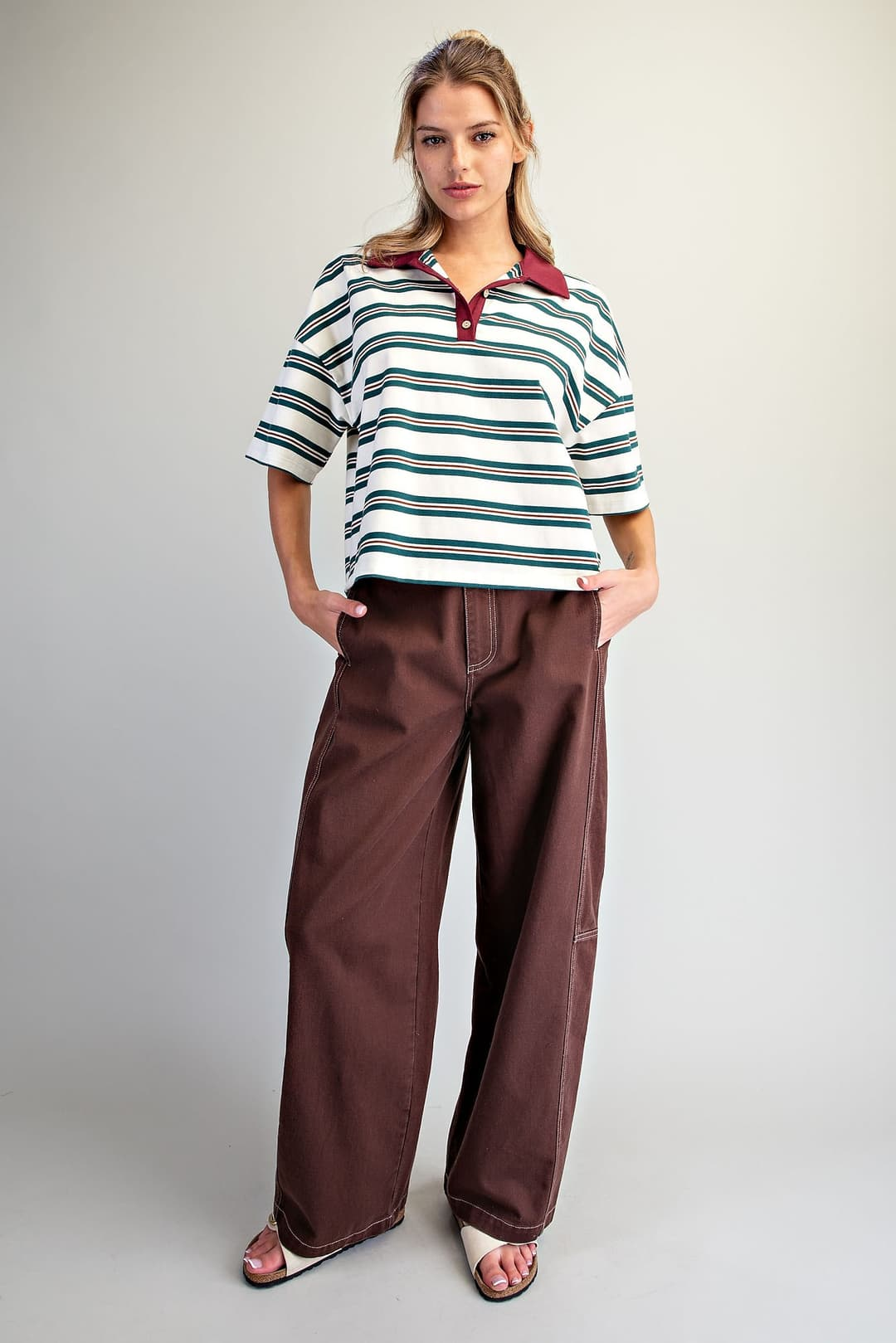 Woman wearing the Cecilia Forest striped oversized polo top with a contrast collar and brown pants.