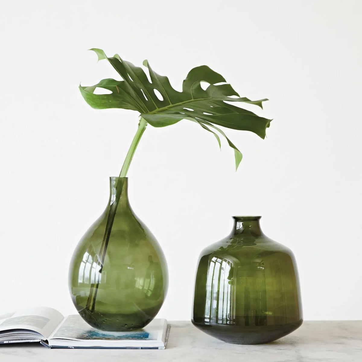 Large round green glass vase with a smooth cylindrical silhouette.
