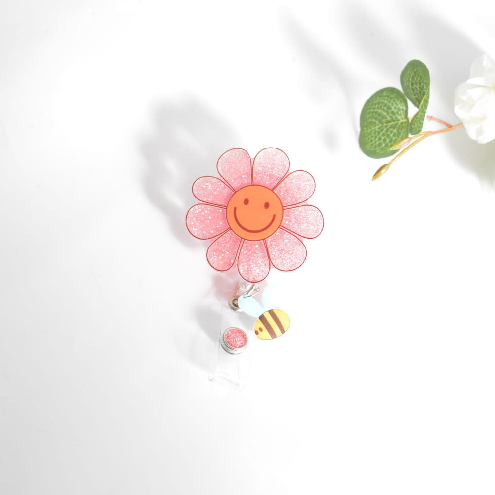 Glitterific badge reel featuring a smiley flower with bee pattern in glitter resin on an alligator clip.