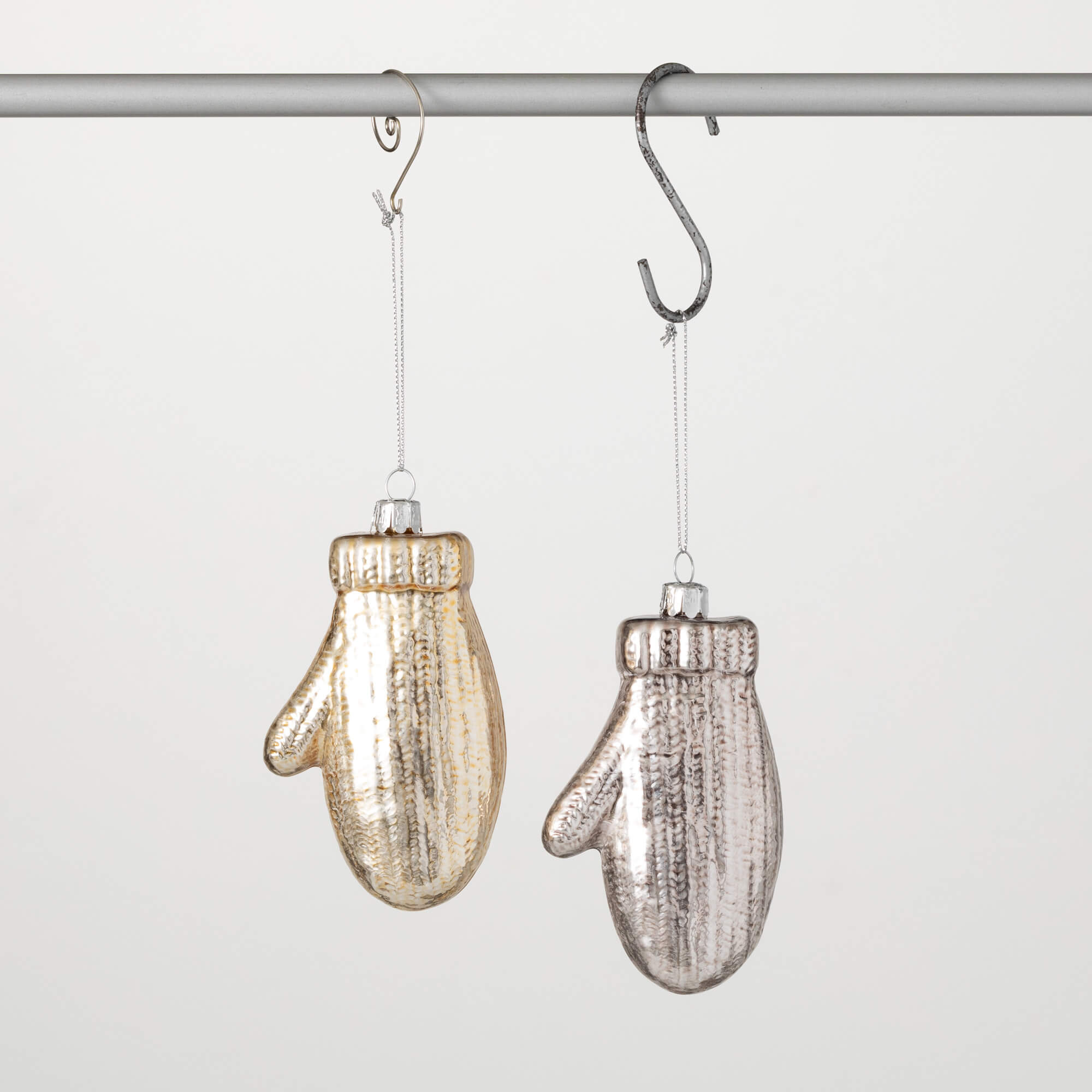 Two glass mitten ornaments in gold and silver hanging from a metal rod.