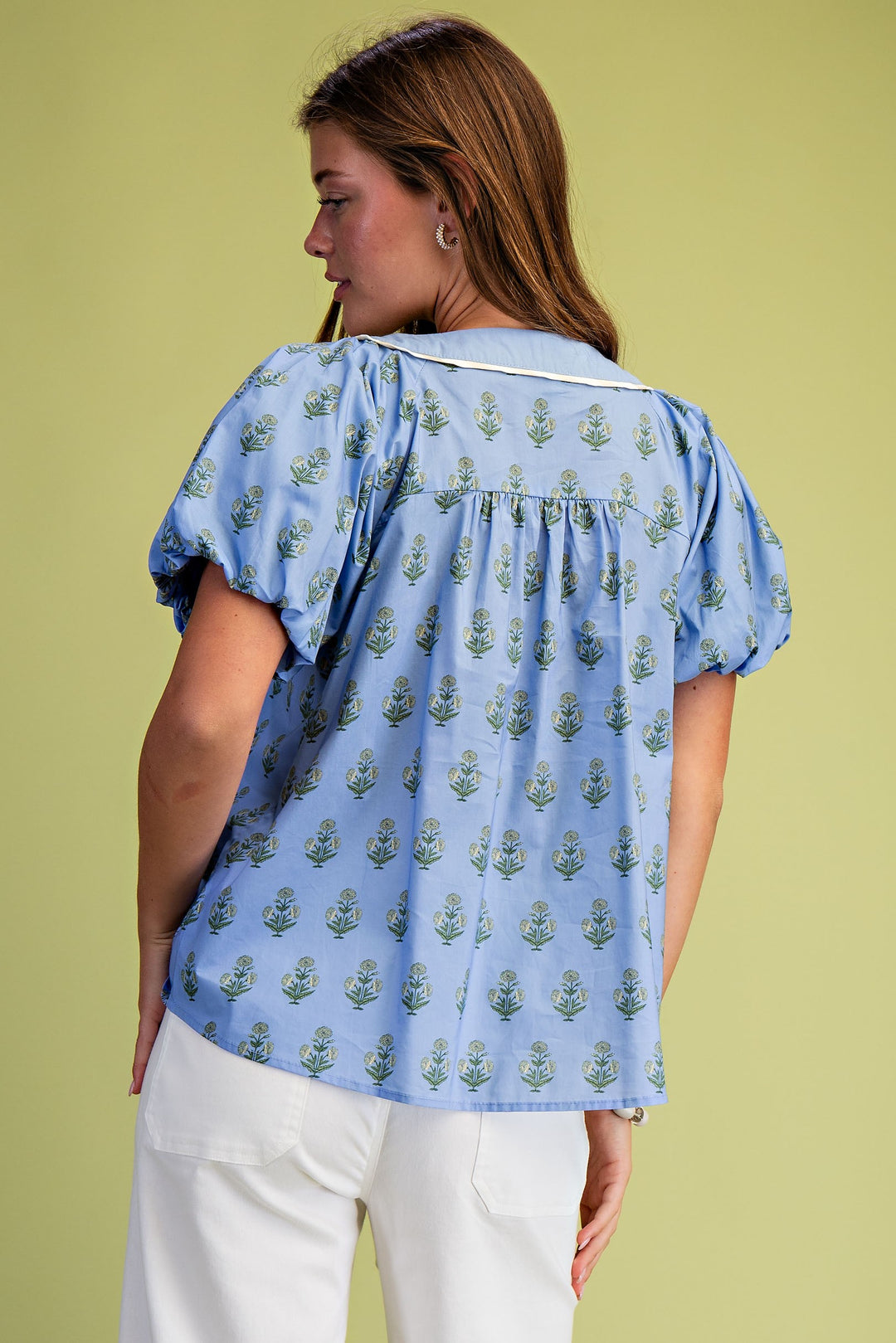 Back view of a woman wearing a blue floral printed pleated blouse with short puff sleeves.
