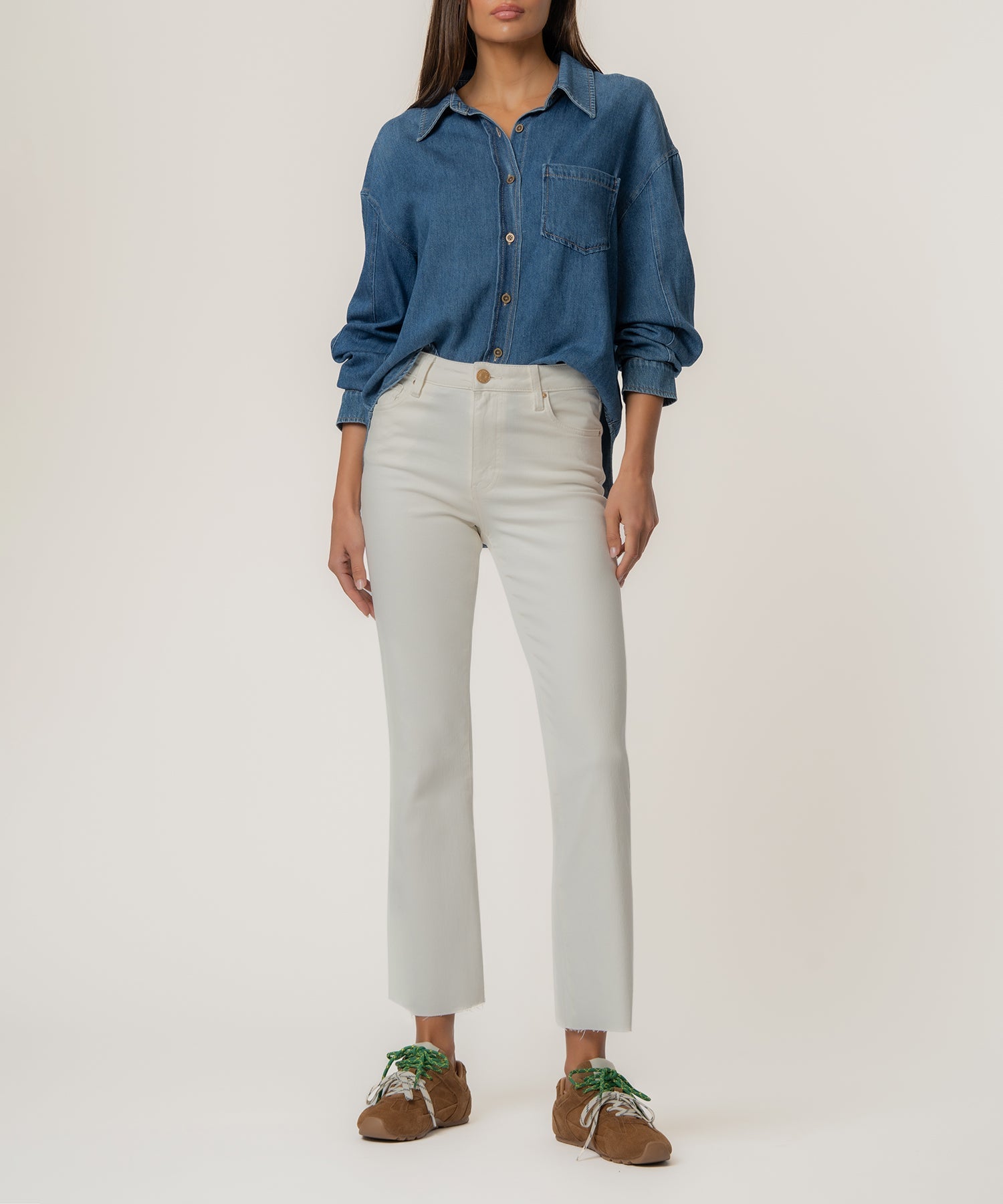 Woman wearing Kelsey high-rise ankle flare jeans in white with a raw hem and a denim shirt.