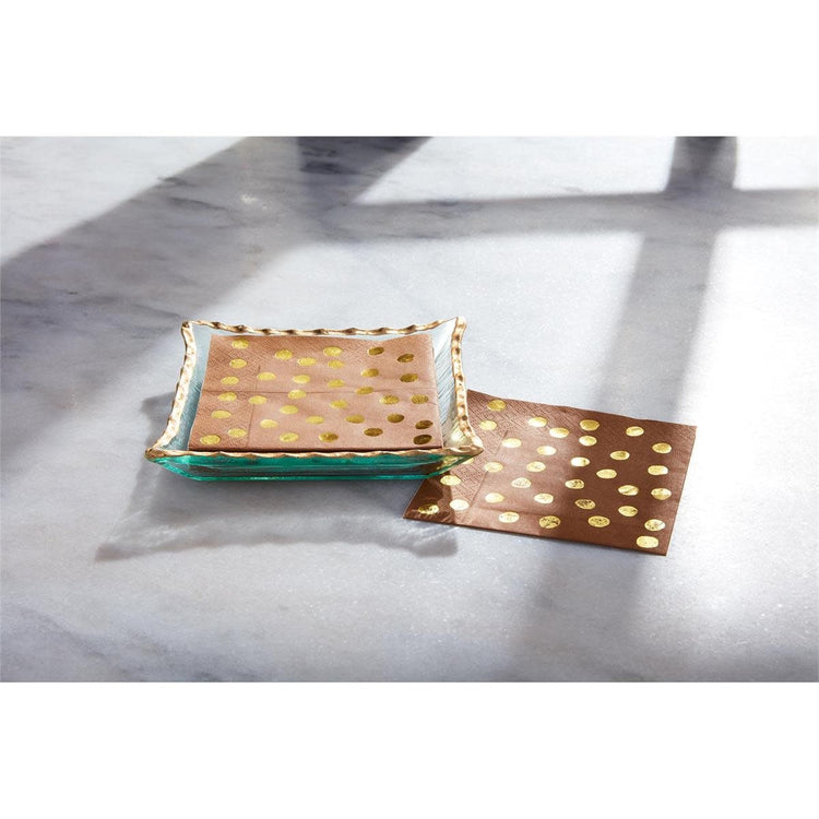 Glass napkin caddy with gold trim holding white square cocktail napkins