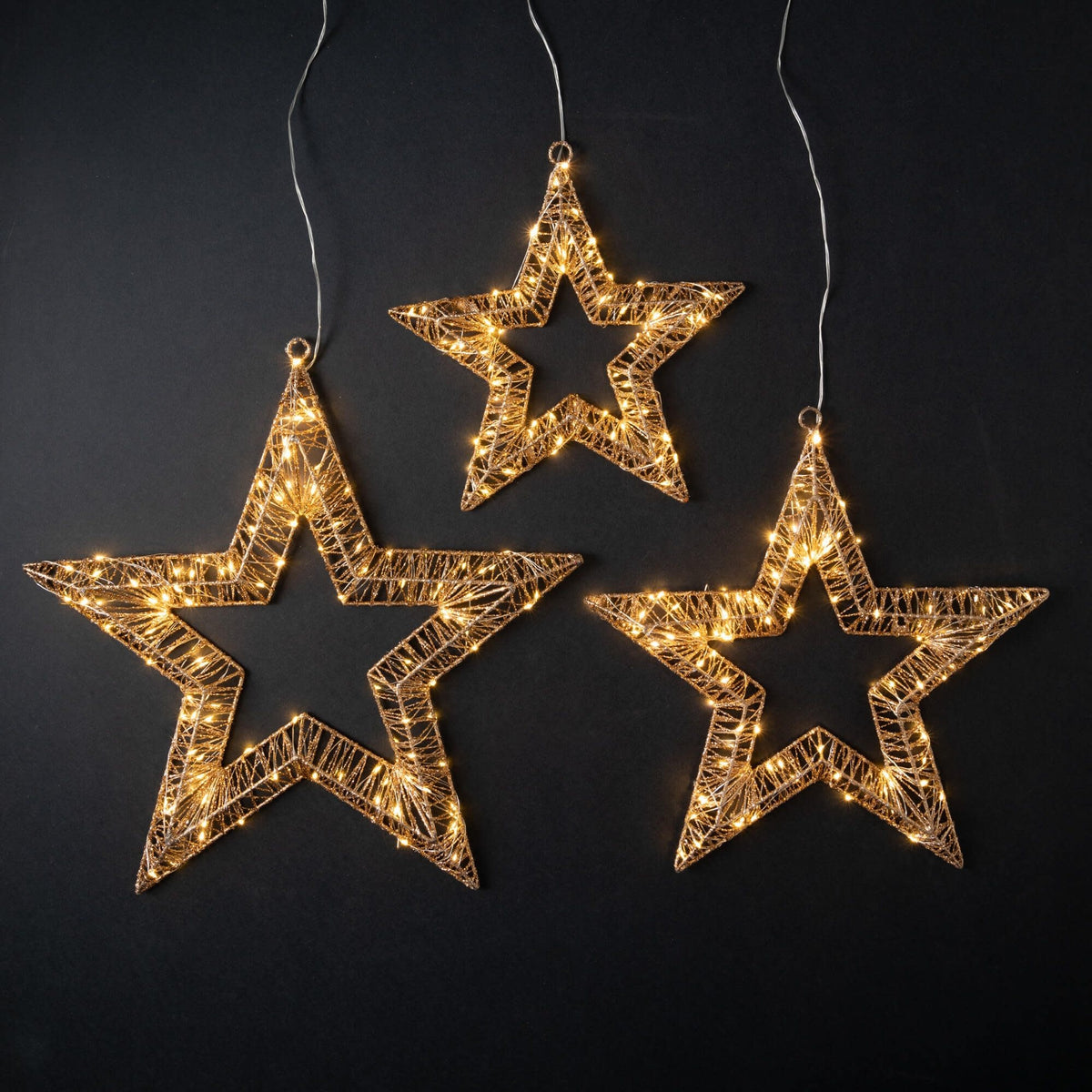 Three gold metal star-shaped lights with warm white LEDs on a black background.