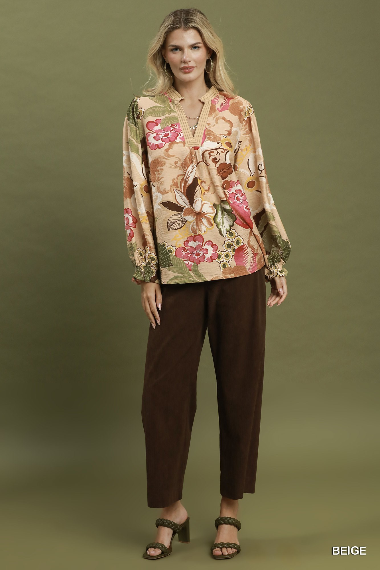 Woman wearing a Mia Floral Print V-Neck Blouse in beige with brown trousers and olive heels.