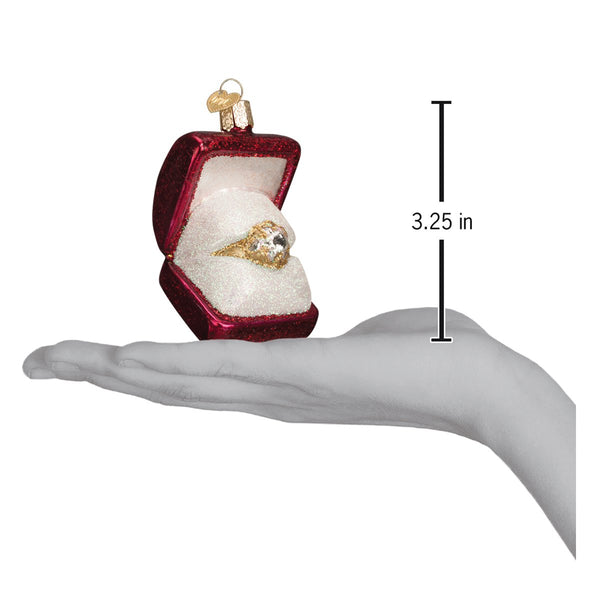 Red glittery ring box ornament with a gold and diamond ring inside, shown held in a hand.