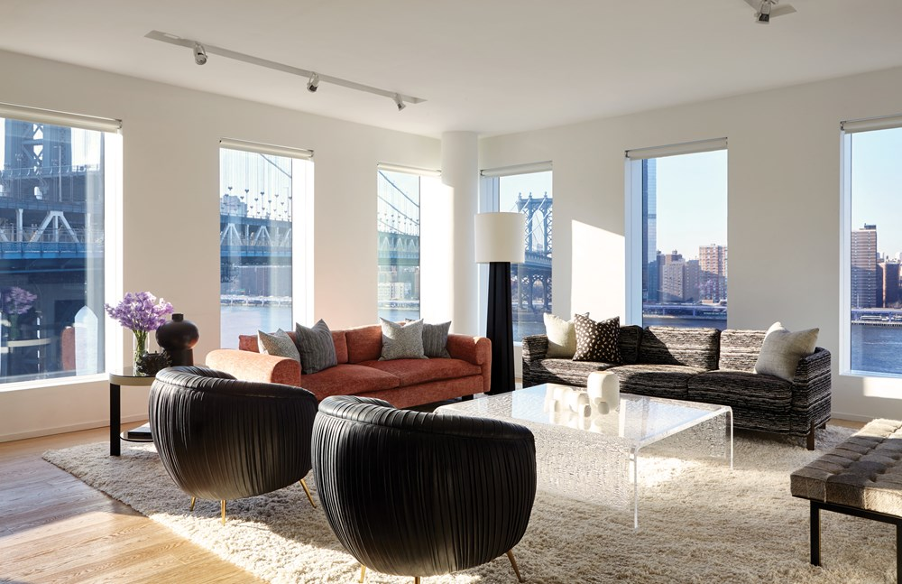 Modern living room with colorful sofas, textured armchairs, and large windows overlooking a bridge.