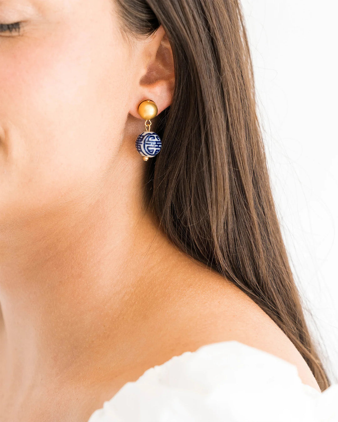 A woman wearing a Blue & White Margaret Drop Earring with a gold stud and patterned ceramic bead.