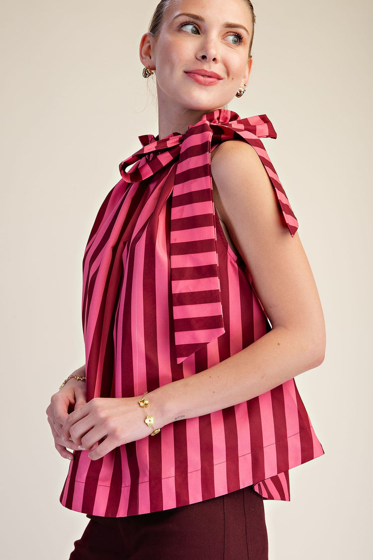 Woman wearing a pink and burgundy striped sleeveless top with a large ruffle neck tie bow.