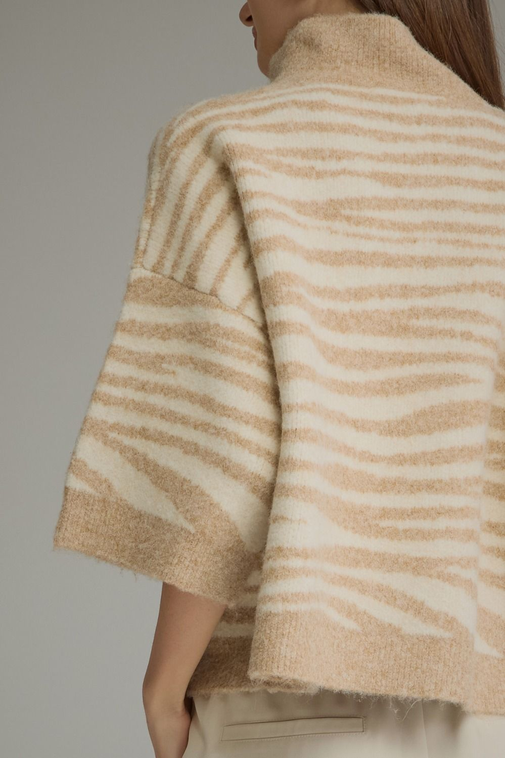 Back view of a woman wearing a beige and cream abstract animal print knit top with 3/4 sleeves.