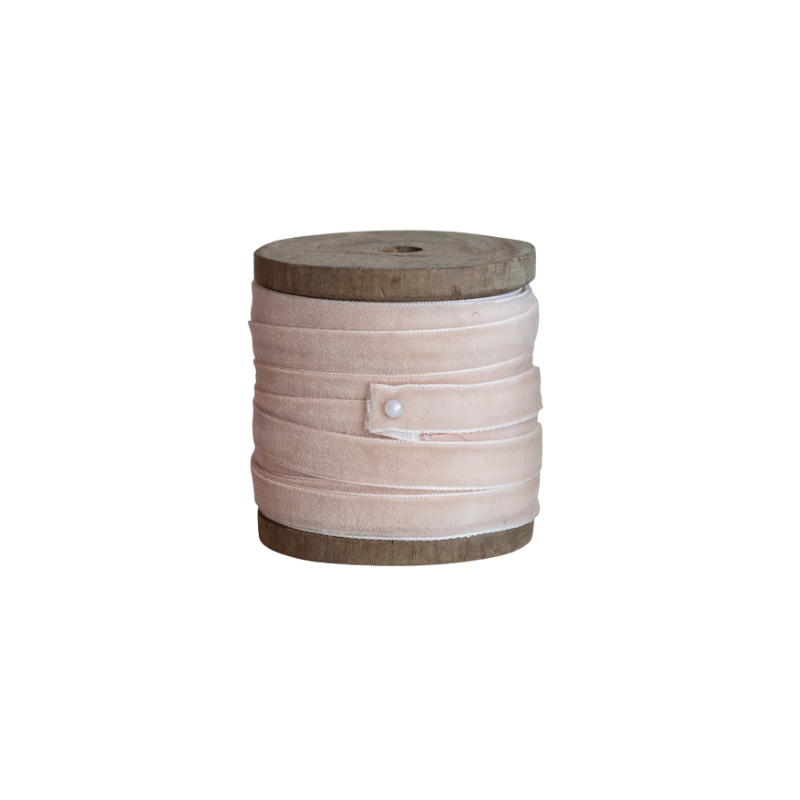 Blush pink 1/4 inch velvet ribbon wrapped around a rustic wooden spool, secured with a pearl pin.