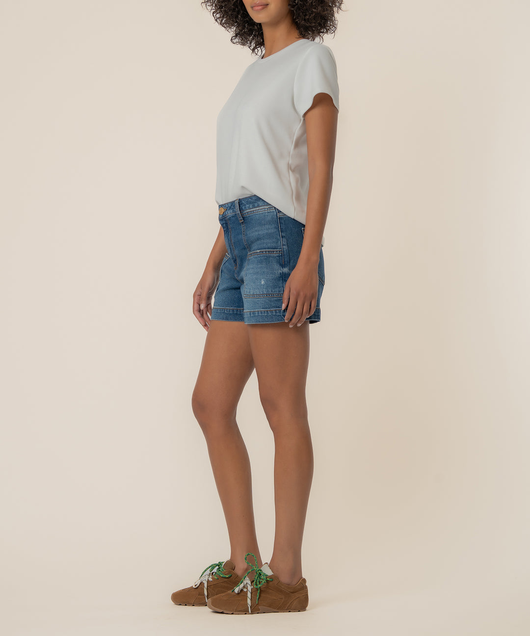Side view of a person wearing Jane high rise denim shorts with pork chop pockets and a white tee.