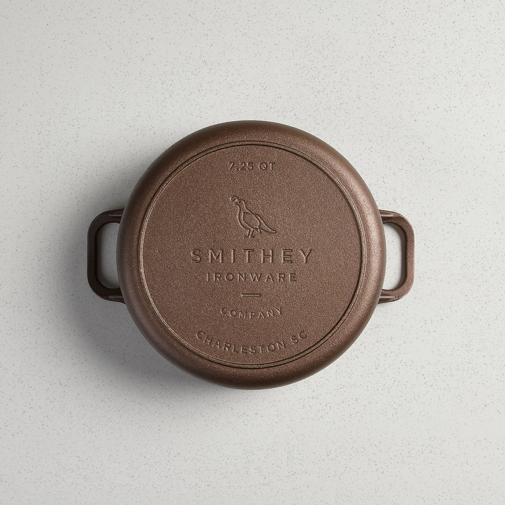 Bottom view of a 7.25 QT Smithey Ironware Dutch Oven in cast iron with engraved logo and handles.