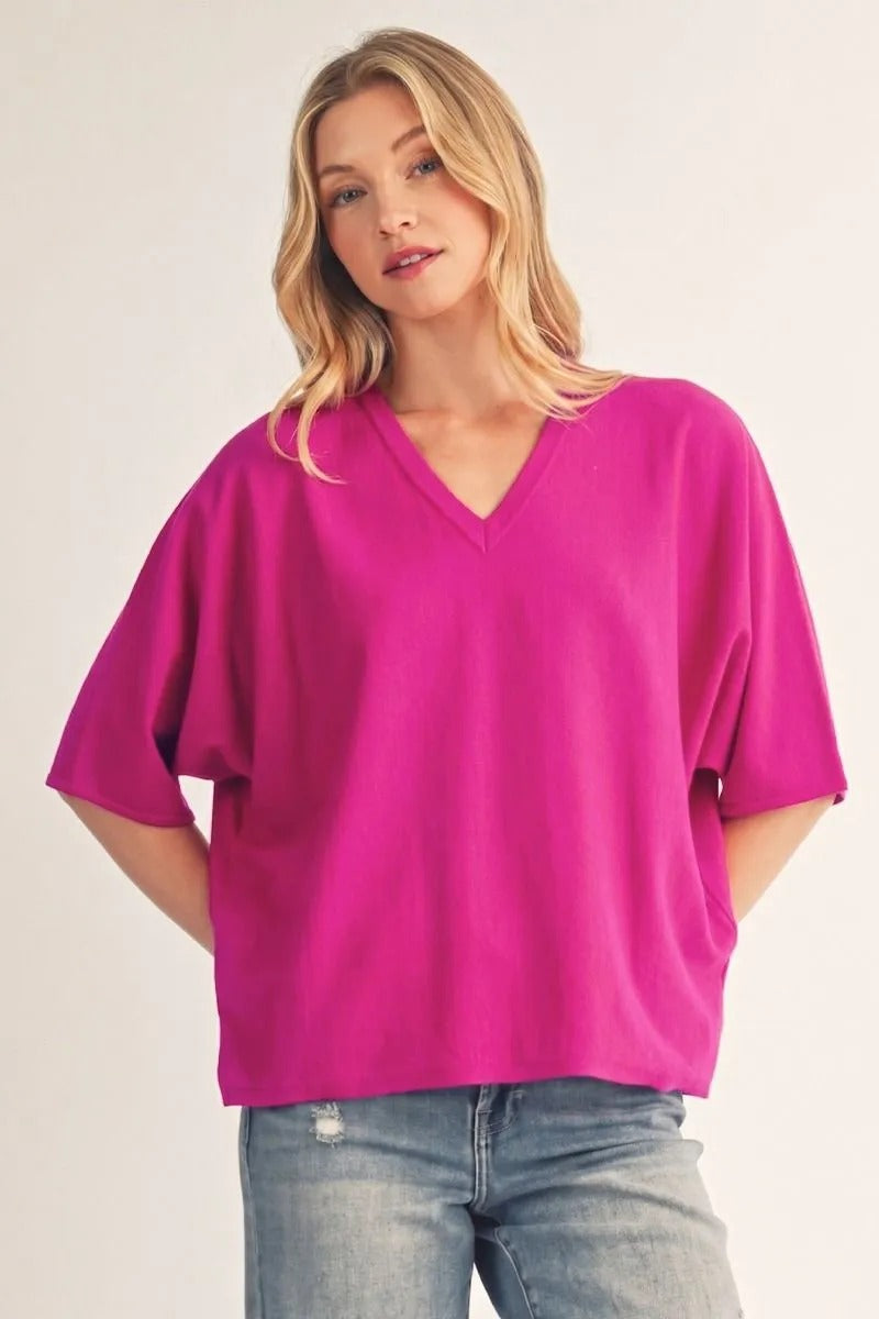 Woman wearing a magenta Ariana drop shoulder V-neck lightweight sweater top with blue jeans.