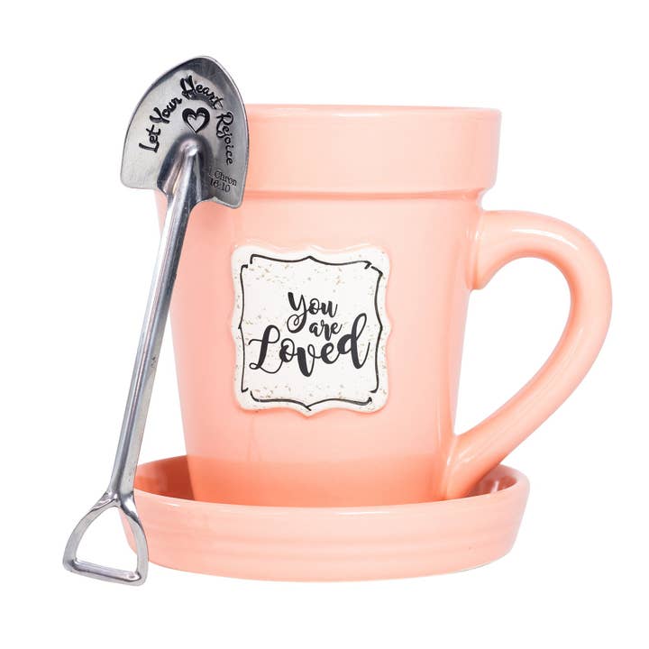 White ceramic mug shaped like a flower pot with saucer lid and stainless steel garden spade spoon.
