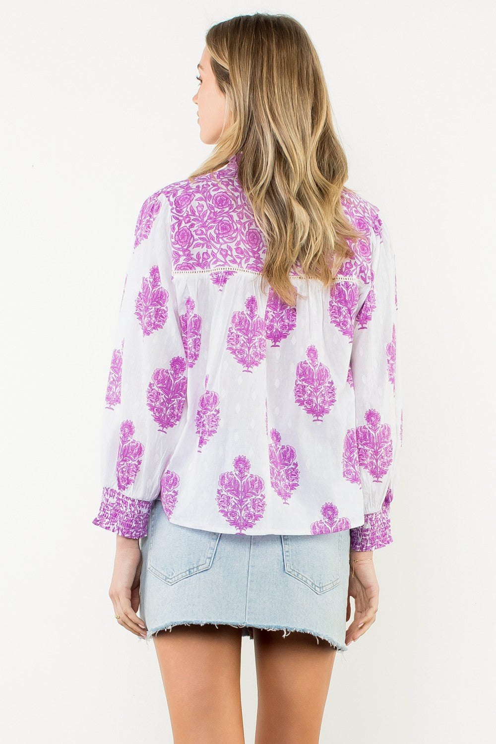 Back view of a woman wearing the Amy Long Sleeve Flower Print Top in white and purple.